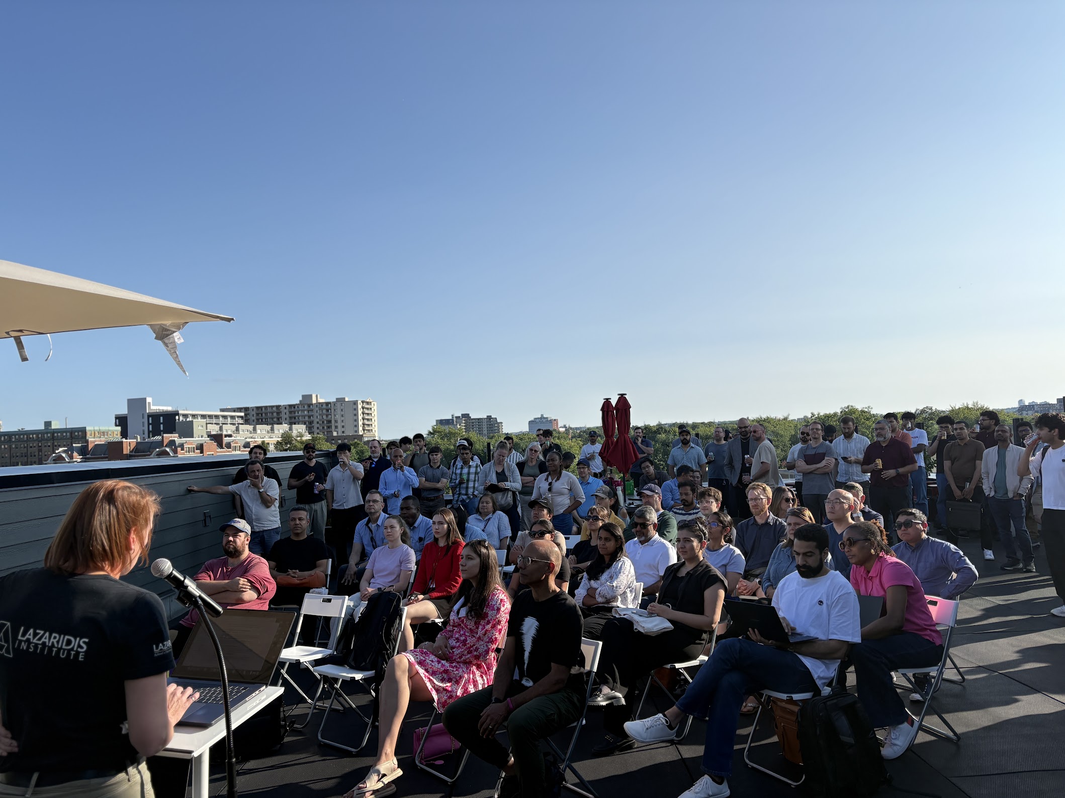 Heather Gawel presenting to a full rooftop crowd at Claude Code for Everyone in downtown Kitchener, with the city skyline behind.
